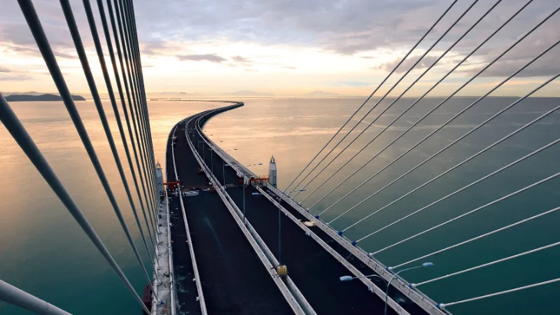Cable-stayed bridge curving out over open water at dusk, seen from the tower